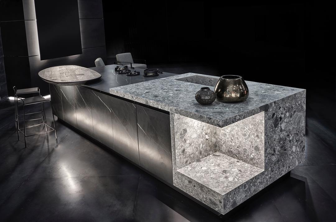 Speckled stone kitchen island with waterfall edges and a recessed open shelf